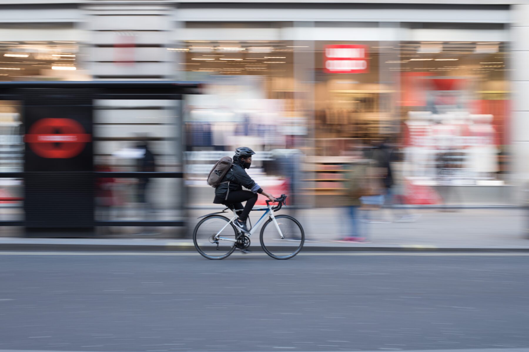 A bicyclist riding on a city street with blurry storefronts in the background