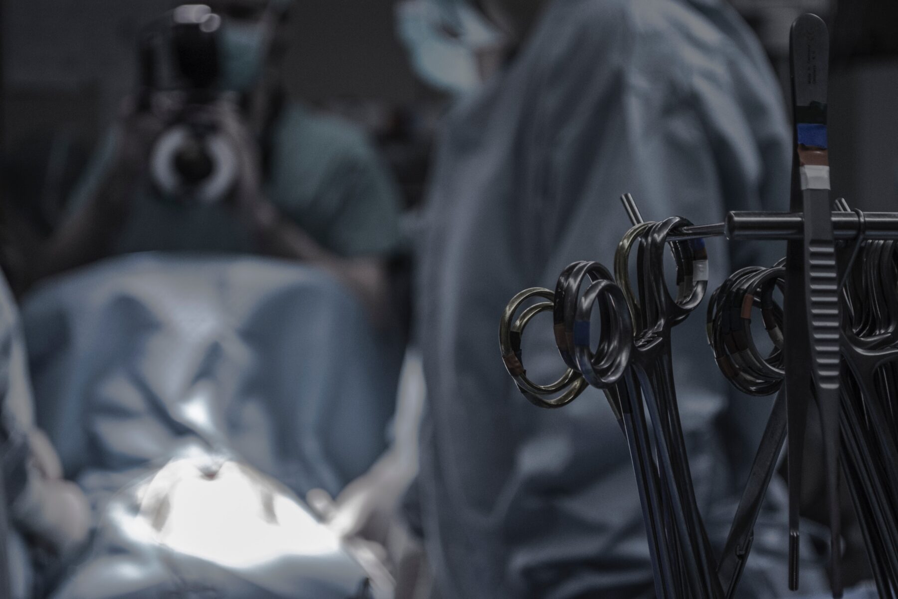 Silver surgical instruments with surgeons in scrubs blurred in the background