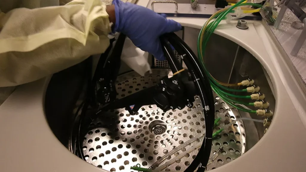 A gloved hand places a duodenoscope into a cleaning device.
