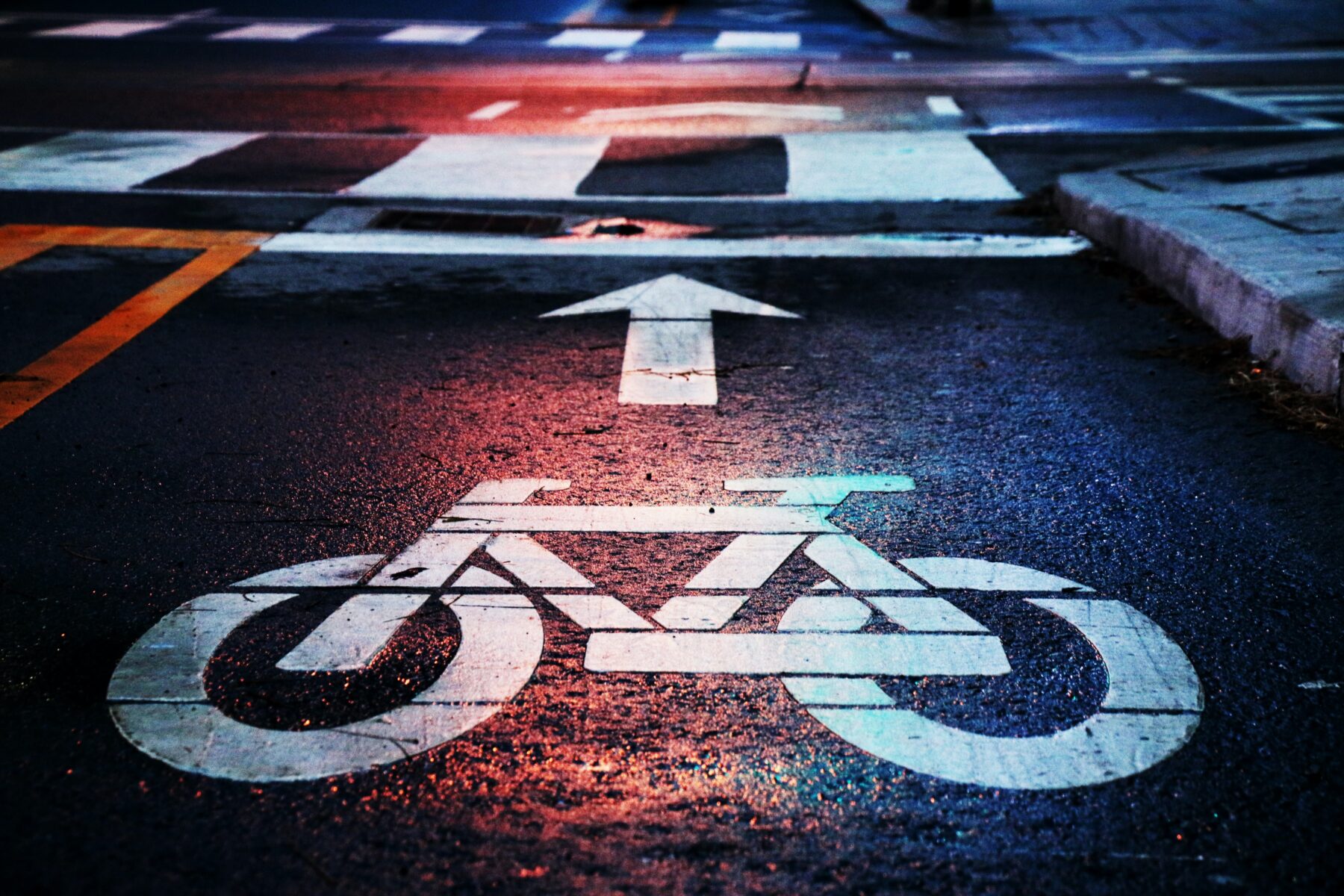 A bike lane intersecting a cross walk, with a white bicycle painted on the black asphalt