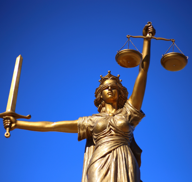 Gold statue of blind Justice holding aloft a sword and scales against a bright blue sky